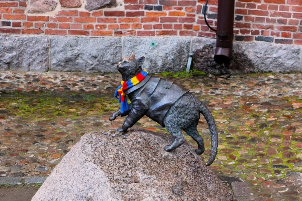 Выборгский замок! Памятник коту Филимону  Памятник коту Филимону — это бронзовая скульптура, установленная в Выборгском замке. Кот Филимон прожил почти 18 лет, из которых 13 лет он провел на Замковом острове, занимая должность «старшего мяучного» сотрудника научного отдела музея. Скульптура изображает кота в пальто, что делает её уникальной среди памятников животным. Филимон был известен как единственный настоящий житель и хозяин замка, который приветствовал гостей, позировал для фотографий и контролировал популяцию грызунов на территории. Он скончался 2 марта 2023 года от неоперабельного рака. Памятник был установлен в память о его вкладе в жизнь замка и его популярности среди посетителей. Эскизы памятника были созданы Лаурой, что добавляет художественную ценность этому объекту. Скульптура стала символом замка и привлекает внимание как местных жителей, так и туристов. Установлен 14.10.2024 г.